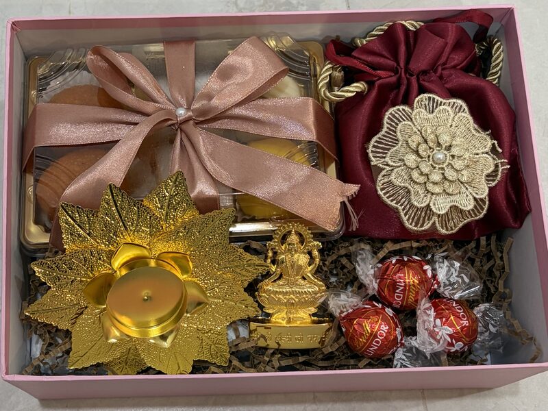 Open pink box with Lakshmi idol, diya, potli and Lindt